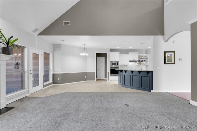 3000 S Tamarack Ave, Broken Arrow, OK 74012 - unfurnished living room with high vaulted ceiling, light tile patterned floors, light colored carpet, a chandelier, and a sink