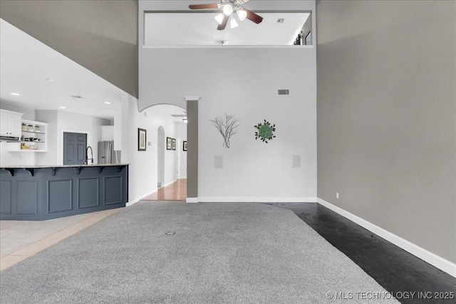 3000 S Tamarack Ave, Broken Arrow, OK 74012 - unfurnished living room with a ceiling fan, arched walkways, a sink, a towering ceiling, and baseboards