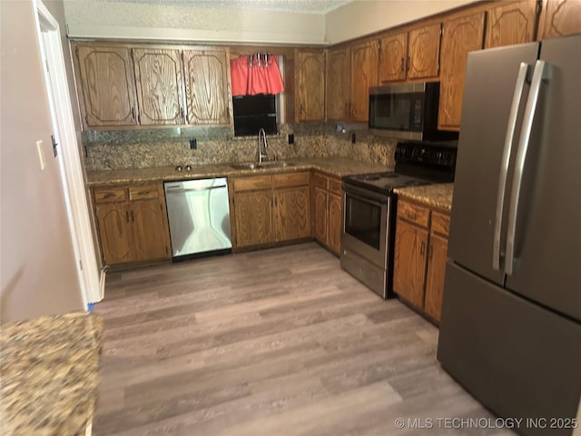 905 Brookside Dr, Durant, OK 74701 - kitchen with appliances with stainless steel finishes, a sink, brown cabinetry, light wood-style flooring, and backsplash