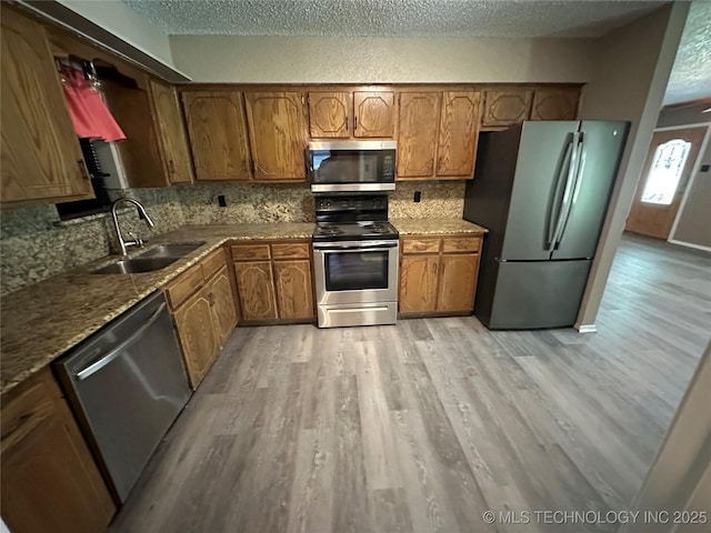 905 Brookside Dr, Durant, OK 74701 - kitchen with stainless steel appliances, a sink, light wood-type flooring, a textured ceiling, and brown cabinets