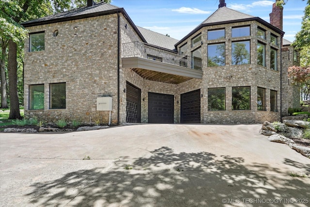5011 E 84th St, Tulsa, OK 74137 - view of front of house with a balcony, a chimney, stone siding, an attached garage, and concrete driveway