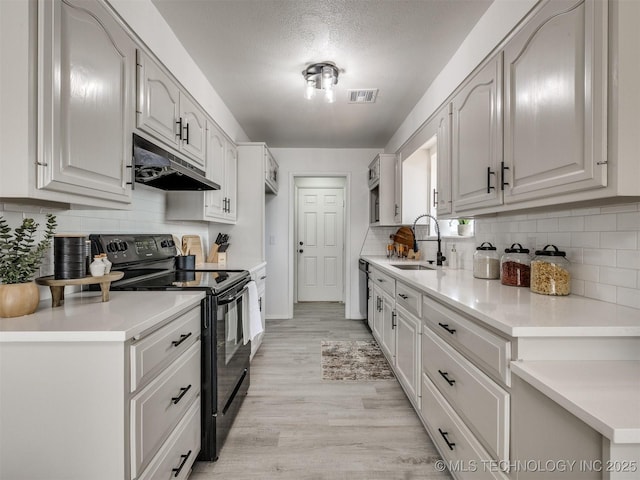 5015 S 89th E Pl, Tulsa, OK 74145 - kitchen with black electric range, under cabinet range hood, decorative backsplash, light wood-style flooring, and a textured ceiling