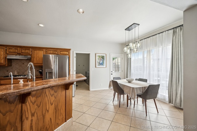 3305 N Oak Ave, Broken Arrow, OK 74012 - kitchen featuring stainless steel refrigerator with ice dispenser, under cabinet range hood, brown cabinetry, light tile patterned flooring, and tasteful backsplash