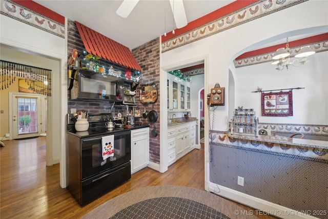 2403 S Troost Ave, Tulsa, OK 74114 - kitchen featuring black appliances, wood finished floors, arched walkways, white cabinetry, and a sink