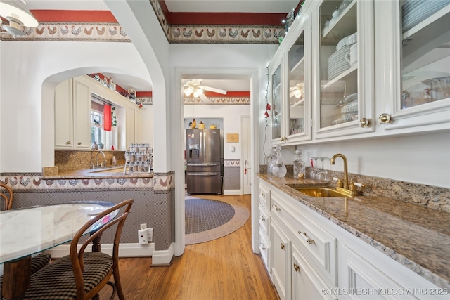 2403 S Troost Ave, Tulsa, OK 74114 - kitchen featuring stainless steel fridge with ice dispenser, a sink, light wood-type flooring, arched walkways, and stone counters