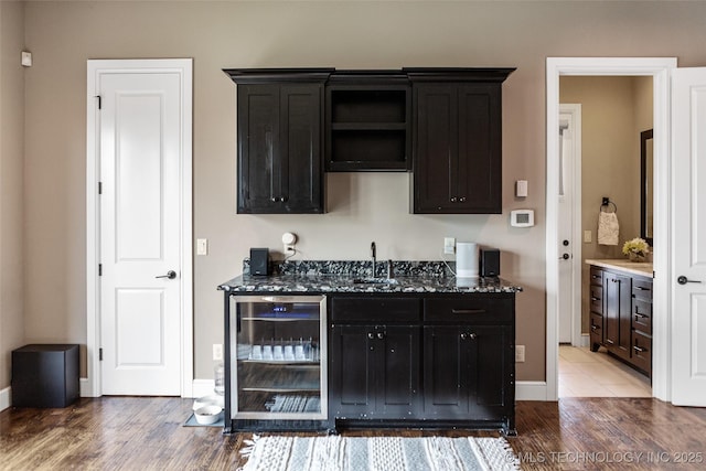 12014 S Kingston Pl, Tulsa, OK 74137 - kitchen with beverage cooler, wood finished floors, dark stone countertops, baseboards, and dark cabinetry