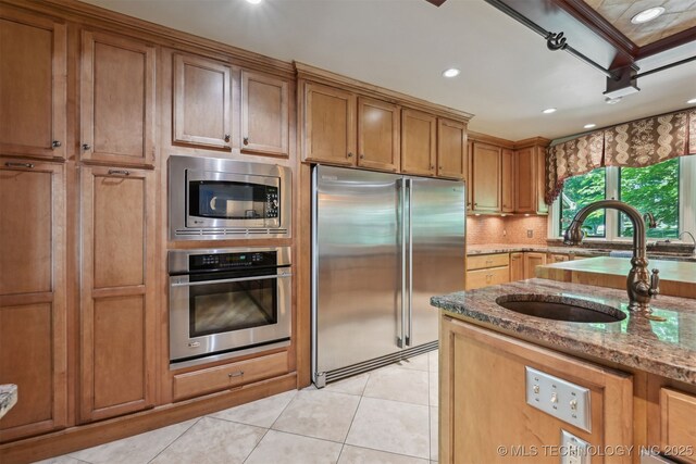 3898 E 72nd St, Tulsa, OK 74136 - kitchen with built in appliances, light tile patterned floors, a sink, brown cabinets, and light stone counters