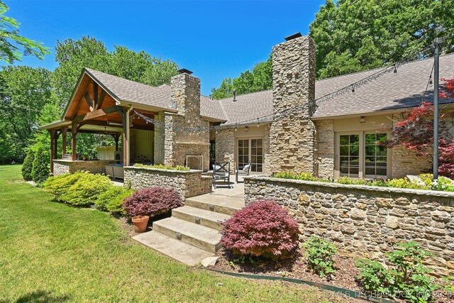 3898 E 72nd St, Tulsa, OK 74136 - view of front of property with stone siding, a chimney, a front yard, a shingled roof, and a patio area
