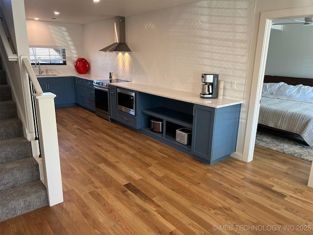56648 Bloomer Rd, Afton, OK 74331 - kitchen featuring stainless steel appliances, wall chimney exhaust hood, blue cabinetry, open shelves, and light wood-style flooring