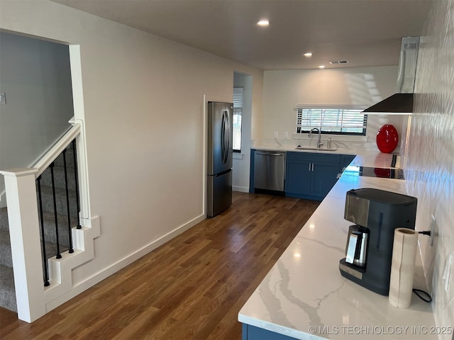 56648 Bloomer Rd, Afton, OK 74331 - kitchen with appliances with stainless steel finishes, a sink, wall chimney exhaust hood, blue cabinetry, and dark wood-style floors