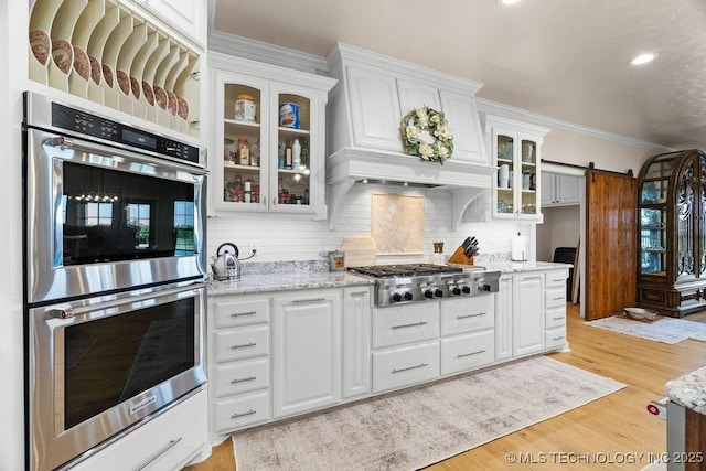 589 Three Mile Rd, Durant, OK 74701 - kitchen with stainless steel appliances, a barn door, backsplash, white cabinetry, and light wood-style floors