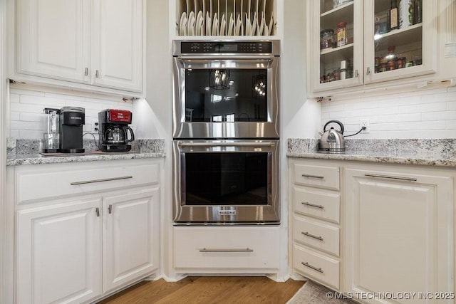 589 Three Mile Rd, Durant, OK 74701 - kitchen featuring double oven, backsplash, glass insert cabinets, white cabinetry, and light stone countertops