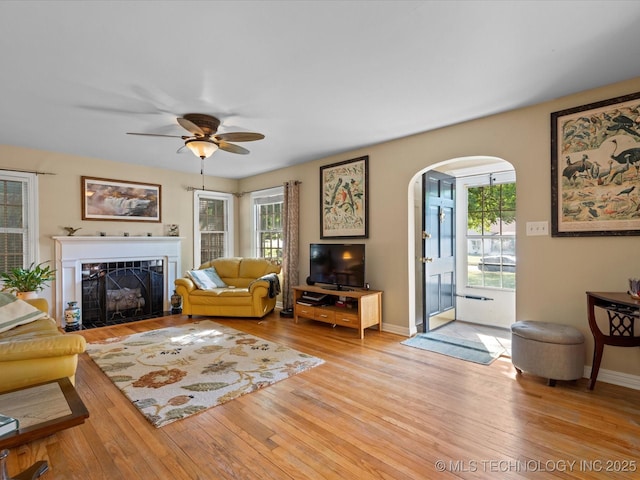 1626 S Dewey Ave, Bartlesville, OK 74003 - living room with arched walkways, ceiling fan, a fireplace with flush hearth, light wood-style flooring, and baseboards