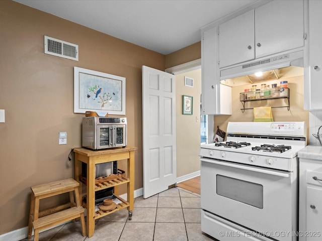 1626 S Dewey Ave, Bartlesville, OK 74003 - kitchen featuring white gas range, under cabinet range hood, light tile patterned floors, light countertops, and white cabinetry