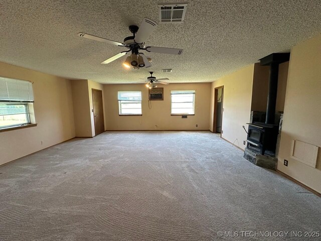 109948 S 4155th Rd, Checotah, OK 74426 - unfurnished living room with a wood stove, a ceiling fan, carpet flooring, a textured ceiling, and baseboards