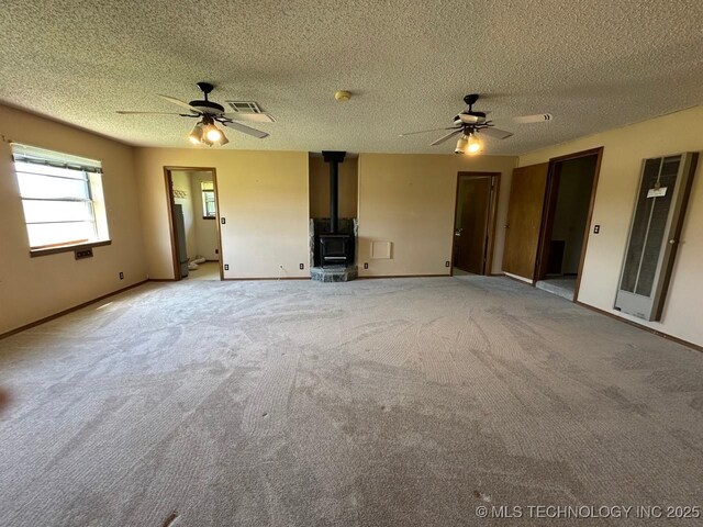 109948 S 4155th Rd, Checotah, OK 74426 - unfurnished living room featuring a wood stove, a ceiling fan, a heating unit, carpet floors, and a textured ceiling