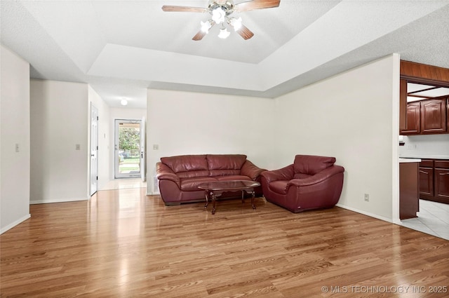 12013 E 27th St, Tulsa, OK 74129 - living room featuring light wood-type flooring, a ceiling fan, a raised ceiling, and baseboards