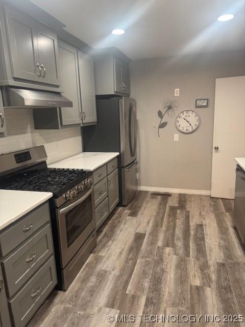 804 W Taliaferro, Madill, OK 73446 - kitchen with appliances with stainless steel finishes, gray cabinets, under cabinet range hood, wood finished floors, and light countertops
