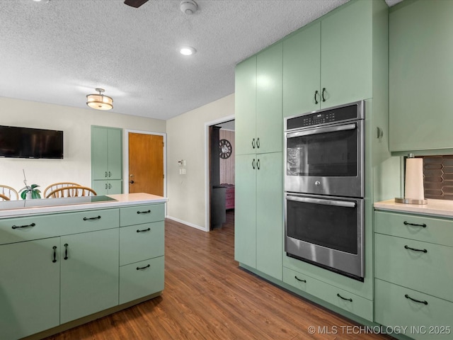 2318 Dorchester Dr, Bartlesville, OK 74006 - kitchen featuring stainless steel double oven, green cabinetry, dark wood-type flooring, a textured ceiling, and light countertops