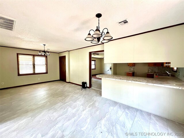 503 NE 4th St, Stigler, OK 74462 - kitchen with a chandelier, white cabinetry, healthy amount of natural light, a textured ceiling, and pendant lighting