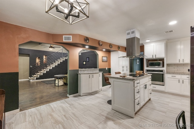 7423 S Urbana Ave, Tulsa, OK 74136 - kitchen featuring appliances with stainless steel finishes, island exhaust hood, white cabinets, backsplash, and light stone counters