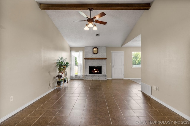 unfurnished living room featuring a ceiling fan, healthy amount of natural light, beam ceiling, baseboards, and a brick fireplace