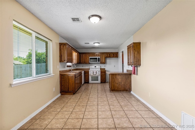 kitchen featuring stainless steel microwave, double oven range, a sink, a textured ceiling, and brown cabinetry