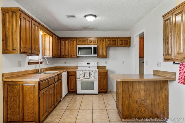 kitchen featuring white appliances, a sink, brown cabinets, a textured ceiling, and light tile patterned floors