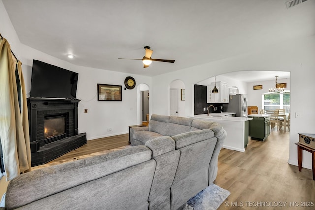 2405 S 13th St, Broken Arrow, OK 74012 - living room with arched walkways, light wood finished floors, a fireplace, a ceiling fan, and a chandelier