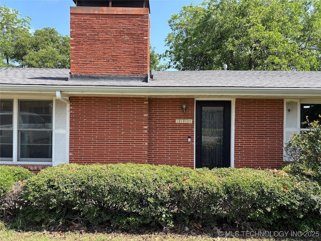 1113 S Meadow Dr, Ardmore, OK 73401 - view of exterior entry with a chimney, brick siding, and roof with shingles