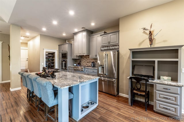 11802 Hickory Ln, Claremore, OK 74017 - kitchen with appliances with stainless steel finishes, gray cabinets, a breakfast bar area, an island with sink, and light stone countertops