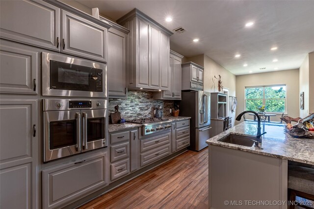 11802 Hickory Ln, Claremore, OK 74017 - kitchen featuring gray cabinets, appliances with stainless steel finishes, dark wood finished floors, light stone counters, and decorative backsplash