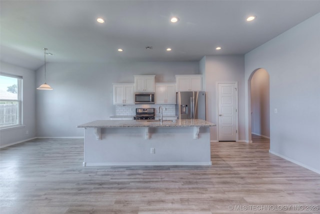 25363 E 87th St S, Broken Arrow, OK 74014 - kitchen featuring appliances with stainless steel finishes, arched walkways, white cabinetry, a kitchen island with sink, and backsplash