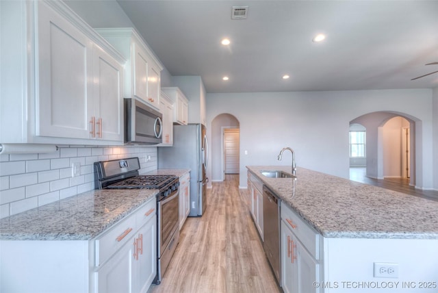 25363 E 87th St S, Broken Arrow, OK 74014 - kitchen with appliances with stainless steel finishes, a sink, arched walkways, white cabinetry, and light wood-type flooring