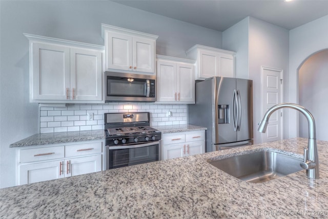 25363 E 87th St S, Broken Arrow, OK 74014 - kitchen with appliances with stainless steel finishes, a sink, white cabinetry, decorative backsplash, and arched walkways