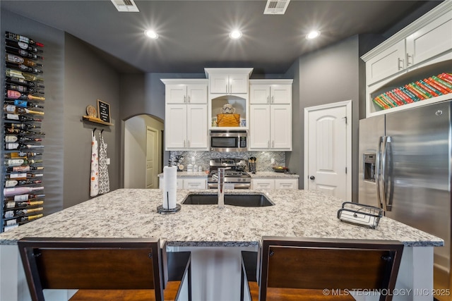 18409 E 50th Pl S, Tulsa, OK 74134 - kitchen with appliances with stainless steel finishes, a kitchen island with sink, arched walkways, white cabinetry, and decorative backsplash