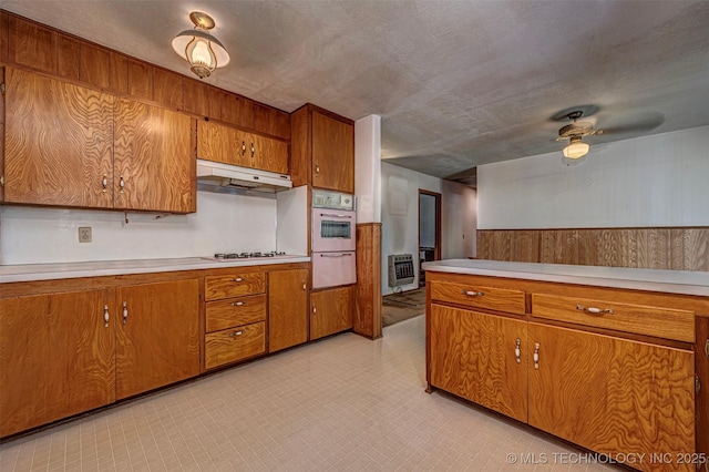 506 S 8th, Davis, OK 73030 - kitchen with brown cabinetry, under cabinet range hood, light countertops, a wainscoted wall, and wooden walls