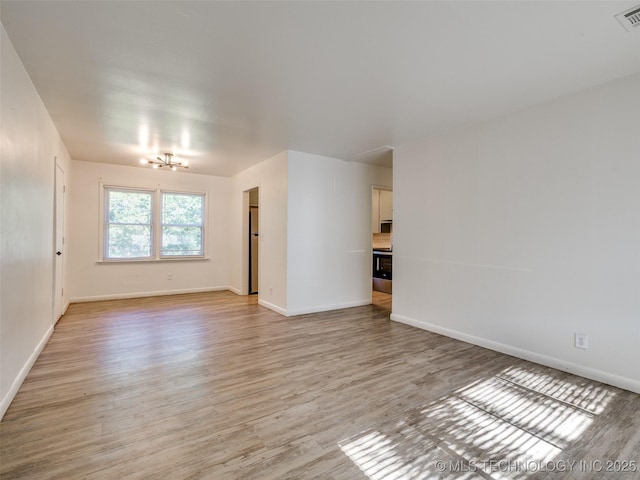 2409 N Urbana Ave, Tulsa, OK 74115 - spare room featuring light wood-style flooring, a chandelier, and baseboards