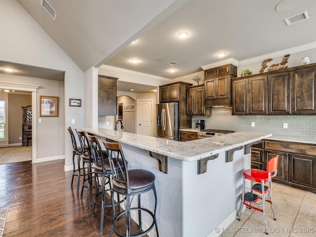 7605 E 82nd Pl, Owasso, OK 74055 - kitchen with stainless steel appliances, a kitchen bar, dark brown cabinets, tasteful backsplash, and ornamental molding