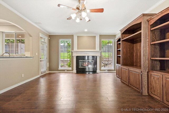 6007 E 76th Ct, Tulsa, OK 74136 - unfurnished living room featuring a glass covered fireplace, ceiling fan, healthy amount of natural light, dark wood-style flooring, and crown molding