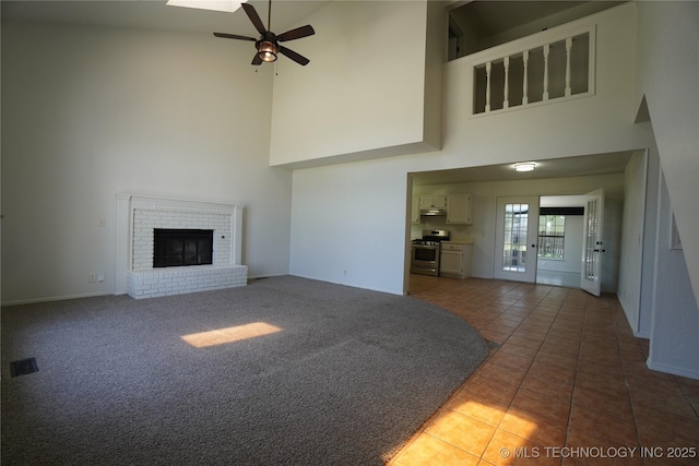 8304 E 124th E Ave, Owasso, OK 74055 - unfurnished living room featuring a towering ceiling, ceiling fan, tile patterned flooring, a brick fireplace, and baseboards