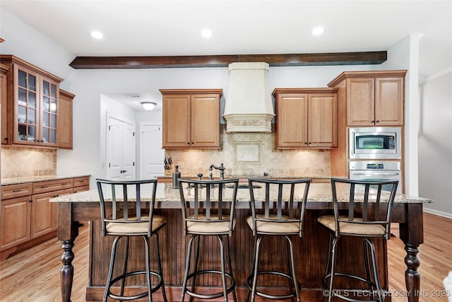 10935 S 77th Pl, Tulsa, OK 74133 - kitchen with custom range hood, stainless steel appliances, decorative backsplash, light stone counters, and an island with sink