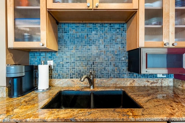 1502 S Boulder Ave Unit 16Cd, Tulsa, OK 74119 - kitchen featuring stainless steel microwave, a sink, glass insert cabinets, backsplash, and light stone countertops