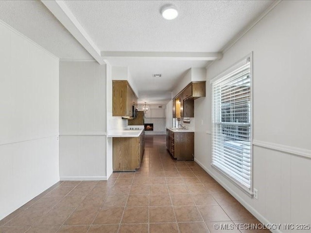 5339 S 32nd W Ave, Tulsa, OK 74107 - kitchen with a textured ceiling, light countertops, light tile patterned floors, brown cabinetry, and a decorative wall