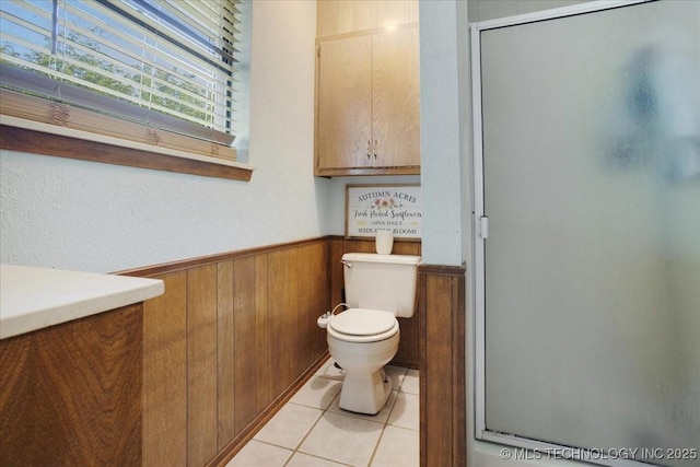 211 Meadowlark, Durant, OK 74701 - bathroom featuring a stall shower, toilet, wood walls, a wainscoted wall, and tile patterned flooring
