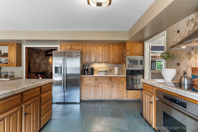 6232 S Jamestown Ave, Tulsa, OK 74136 - kitchen featuring stainless steel appliances, a fireplace, backsplash, dark stone finish floors, and wall chimney exhaust hood