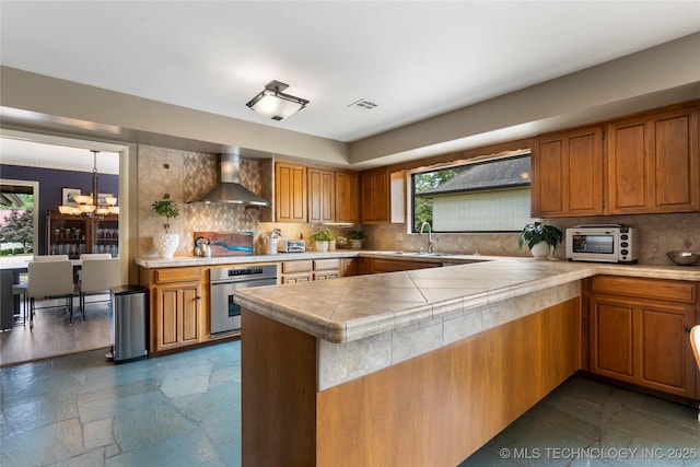 6232 S Jamestown Ave, Tulsa, OK 74136 - kitchen with stainless steel oven, wall chimney exhaust hood, a sink, brown cabinetry, and healthy amount of natural light