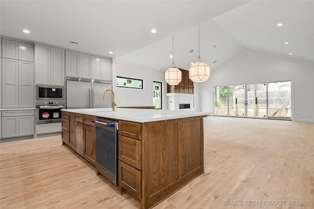 3917 S Madison Ave, Tulsa, OK 74105 - kitchen featuring built in appliances, high vaulted ceiling, light countertops, a kitchen island with sink, and light wood-type flooring