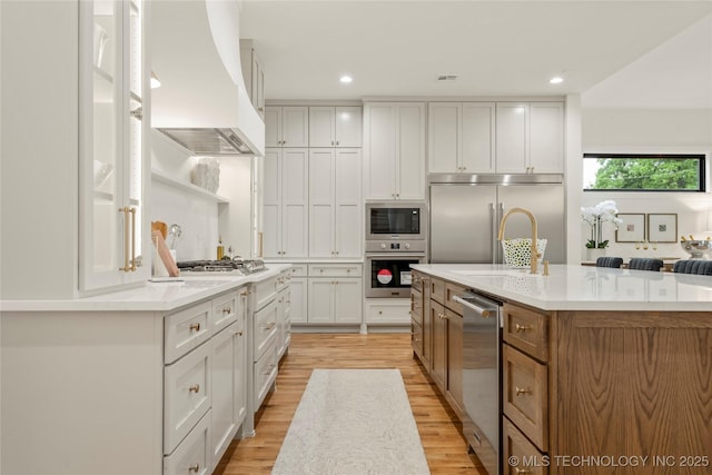 3917 S Madison Ave, Tulsa, OK 74105 - kitchen featuring custom exhaust hood, built in appliances, light wood-style flooring, a spacious island, and white cabinets