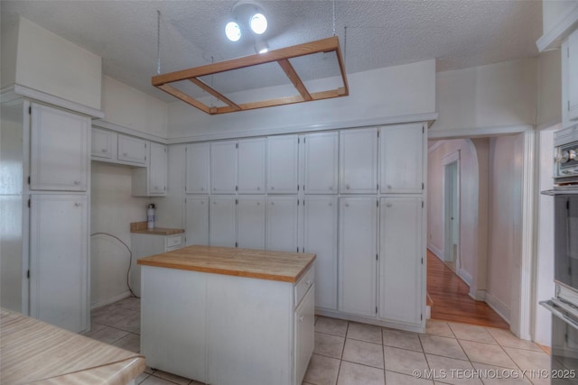 234 E Freeport St, Broken Arrow, OK 74012 - kitchen featuring light tile patterned floors, a center island, white cabinets, wood counters, and a textured ceiling